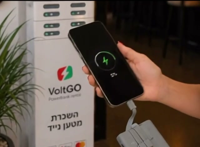 לקוחה טוענת טלפון באמצעות מטען נייד של VoltGo ליד עמדת הטעינה